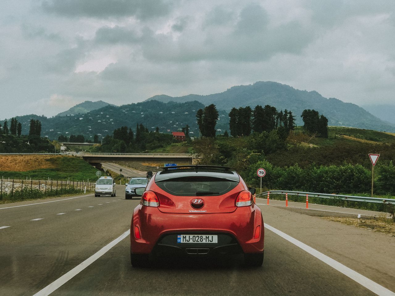 Red Hyundai Veloster travels on a scenic highway in Georgia with lush mountains in the background.